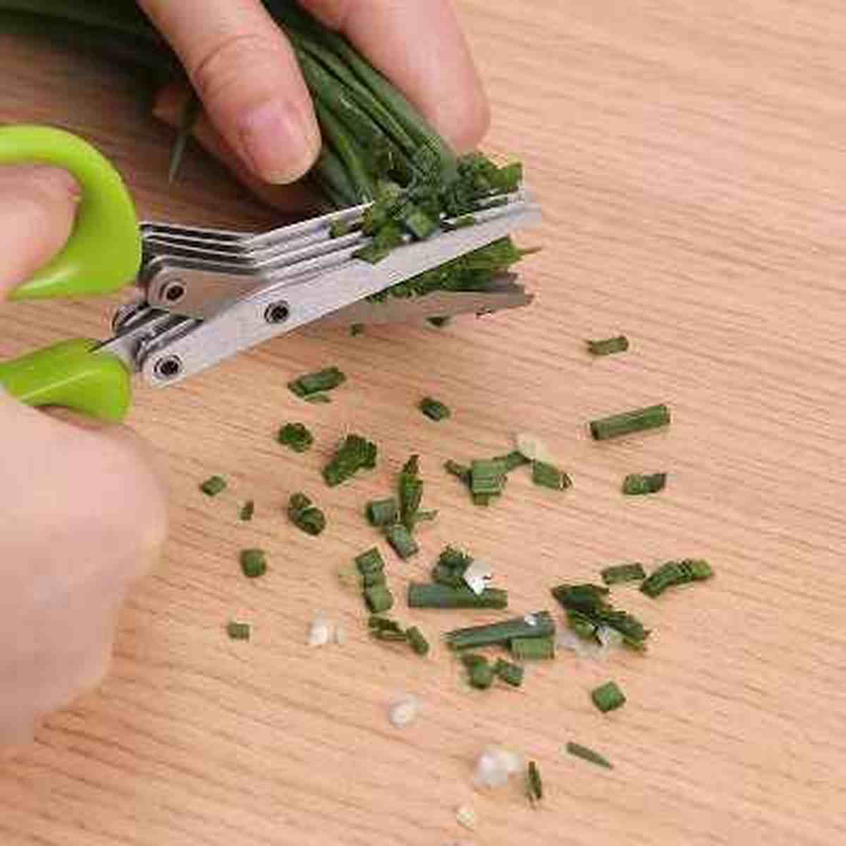 Herbes aromatiques finement ciselées sur une planche en bois grâce aux ciseaux de cuisine 5 lames.