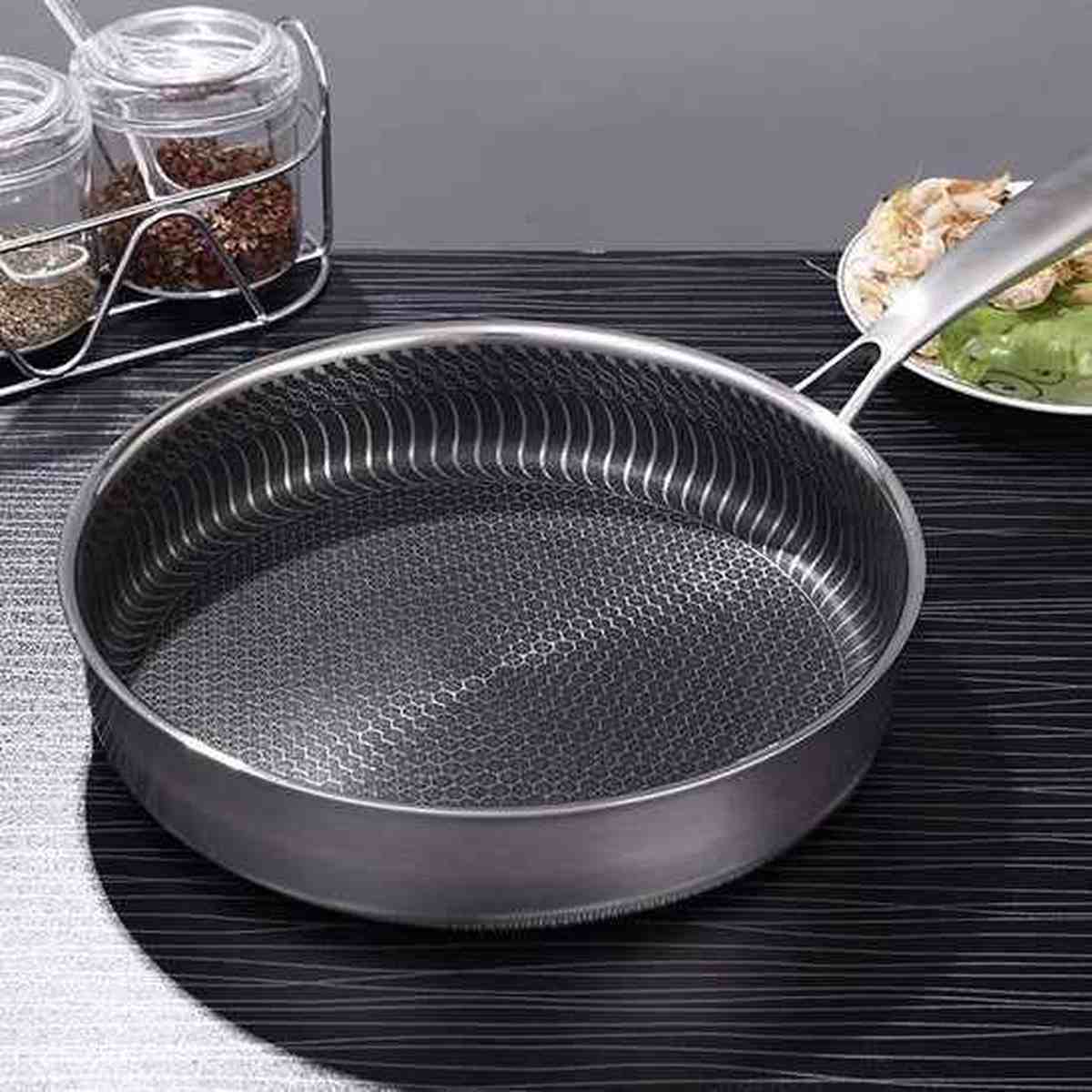 Vue latérale de la poêle en acier inoxydable montrant le manche ergonomique riveté et la structure multicouche haute performance