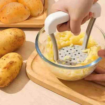 Main utilisant le presse-purée ergonomique en acier inoxydable pour écraser des pommes de terre dans un bol, avec des patates entières en arrière-plan