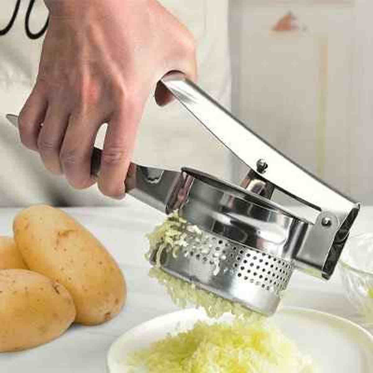 Gros plan d'un presse-purée manuel en inox extrudant une pomme de terre cuite en fins morceaux réguliers pour une texture parfaite.
