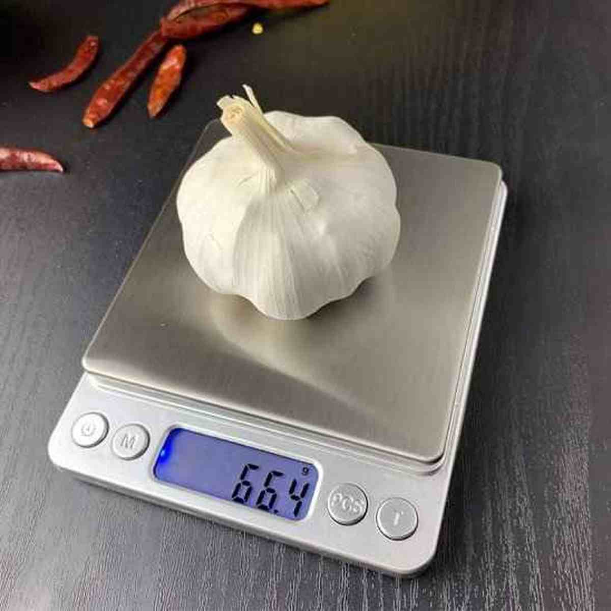 Gousse d'ail posée sur le plateau en acier inoxydable de la balance Cuisinier Parfait, affichant 66.4g sur l'écran LCD bleu.