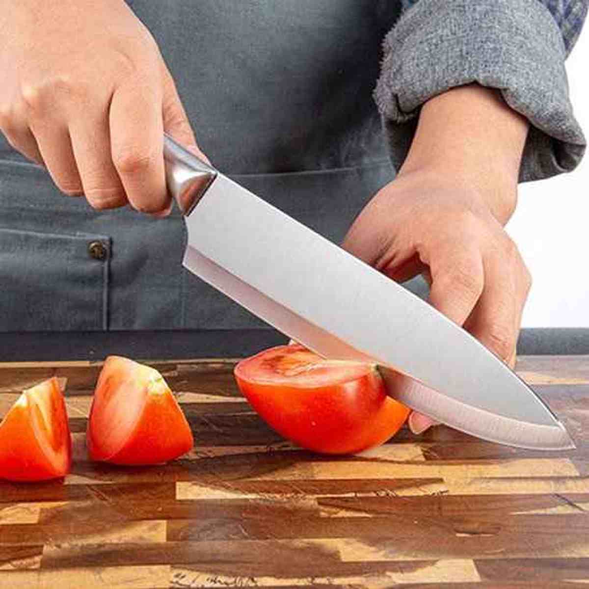 Couteau de chef professionnel en acier inoxydable tranchant une tomate avec précision sur une planche en bois.