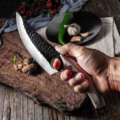 Couteau de chef Ultra-Cut à lame noire martelée tenu au-dessus d'un plan de travail rustique avec légumes frais.