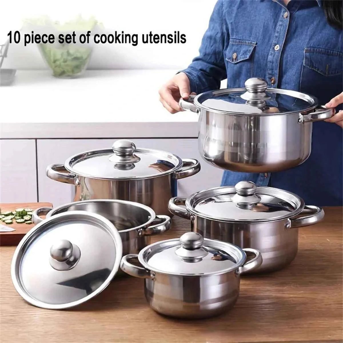 Femme tenant une grande marmite en acier inoxydable issue de l'ensemble de cuisson multifonction avec couvercles en verre.