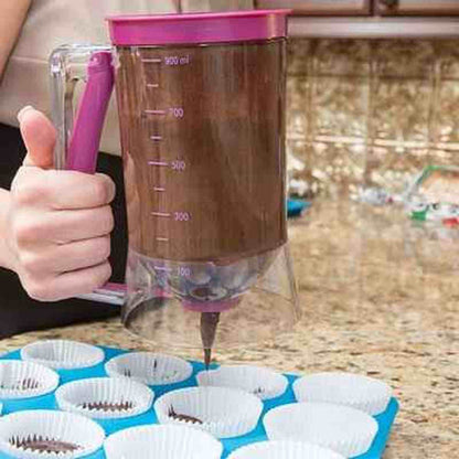 Entonnoir à piston transparent rempli de pâte foncée, dosant avec précision dans des caissettes à muffins blanches sur un plan de travail en granit.