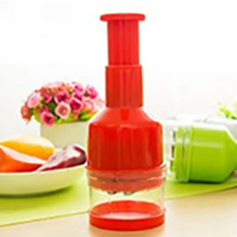 Hachoir manuel à pression rouge pour oignons et ail avec accessoires sur un plan de travail de cuisine.