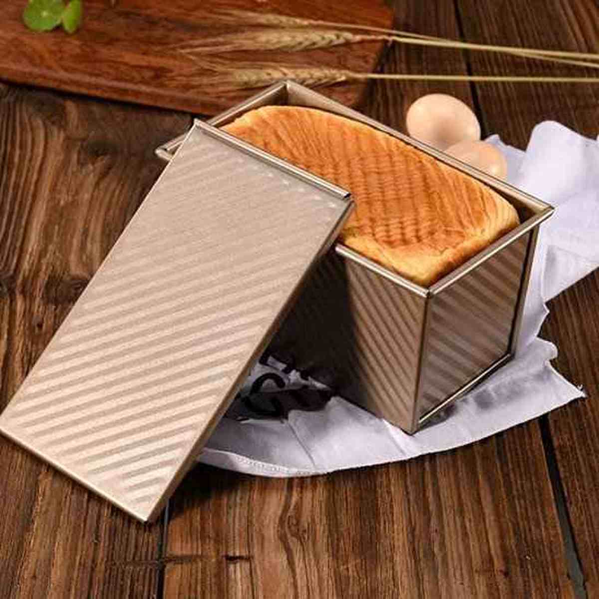 Pain de mie maison parfaitement doré cuit dans le moule à pain PâtissiPro avec couvercle, posé sur un plan de travail en bois.