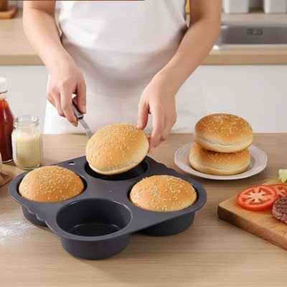 Démoulage d'un pain burger fait maison d'un moule en silicone noir AntiadhésifPro, avec des ingrédients frais pour burger en arrière-plan.