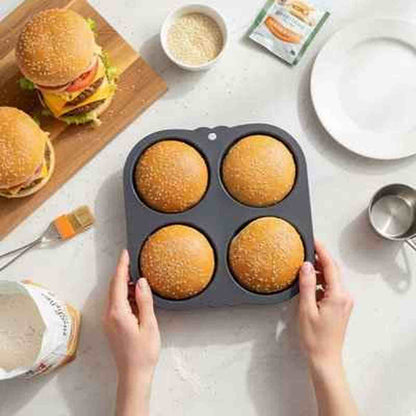Vue de dessus d'un moule à pains burger en silicone noir AntiadhésifPro contenant des pains dorés, entouré de farine et d'accessoires de boulangerie.