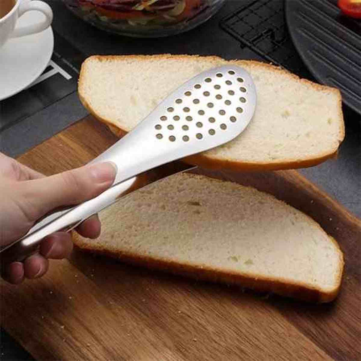 Pince de cuisine en acier inoxydable avec tête perforée saisissant une tranche de pain de mie, démontrant la précision et la douceur du contrôle.
