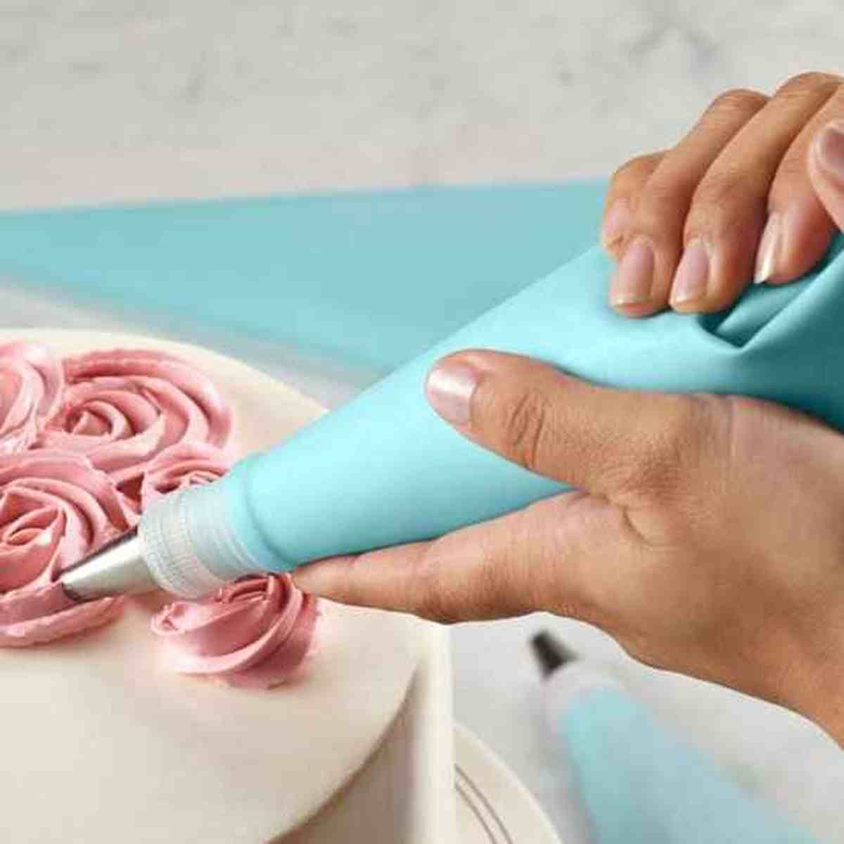 Utilisation d'une poche à douille en silicone bleu PâtissiPro pour décorer un gâteau avec des roses en crème rose, montrant la précision du kit professionnel.