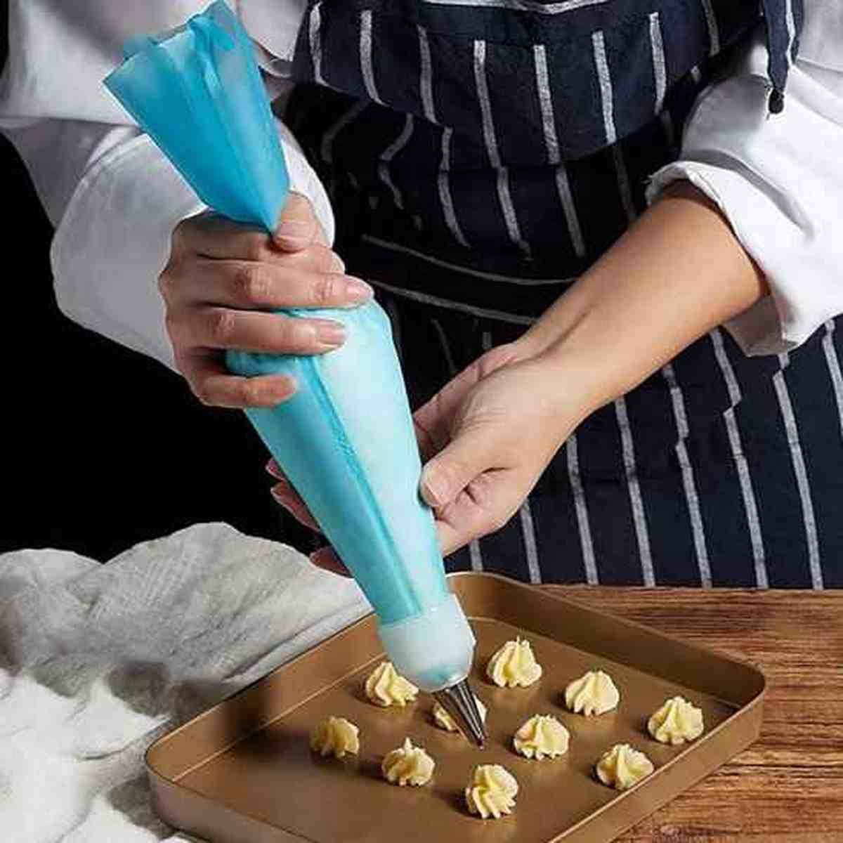 Dressage de petits fours sur une plaque de cuisson avec la poche à douille en silicone bleu PâtissiPro, illustrant sa précision et sa polyvalence