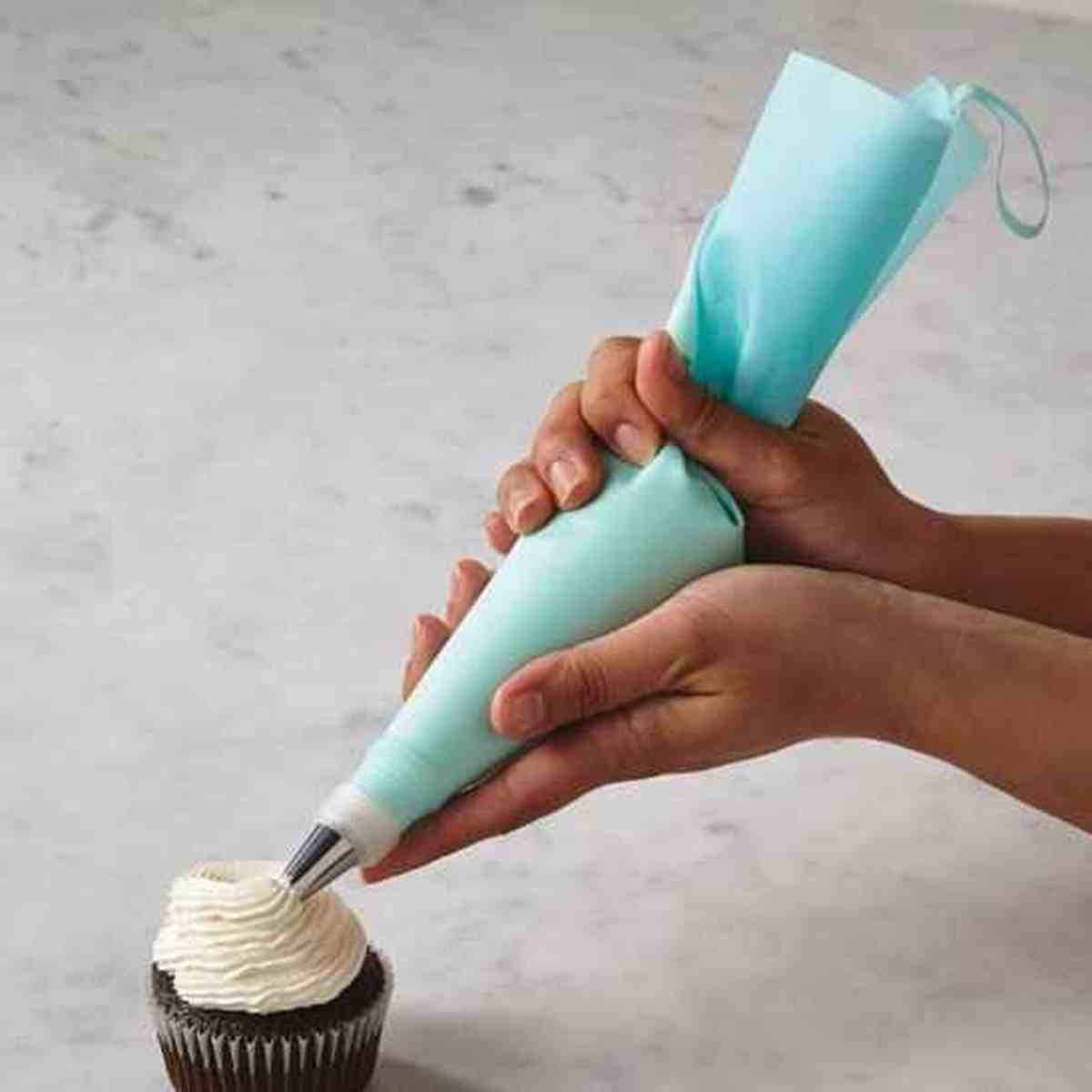 Décoration d'un cupcake au chocolat avec une poche à douille en silicone bleu PâtissiPro, montrant la facilité de prise en main et la précision du glaçage.