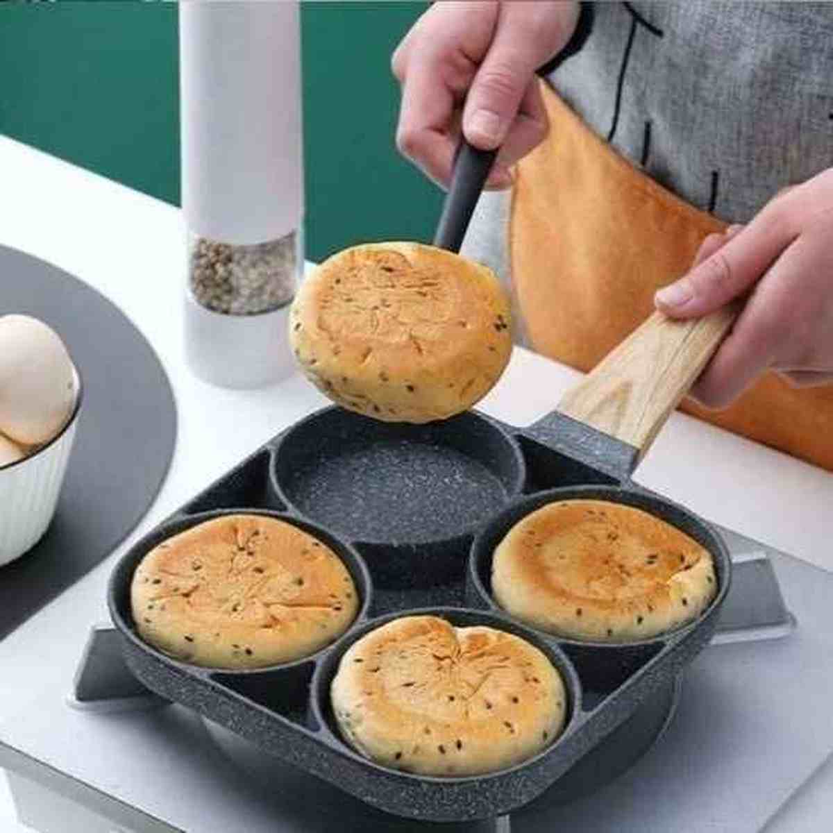 Petits pains maison dorés cuisant dans les compartiments d'une poêle PerfectCook, montrant la hauteur des bords pour des formes régulières.