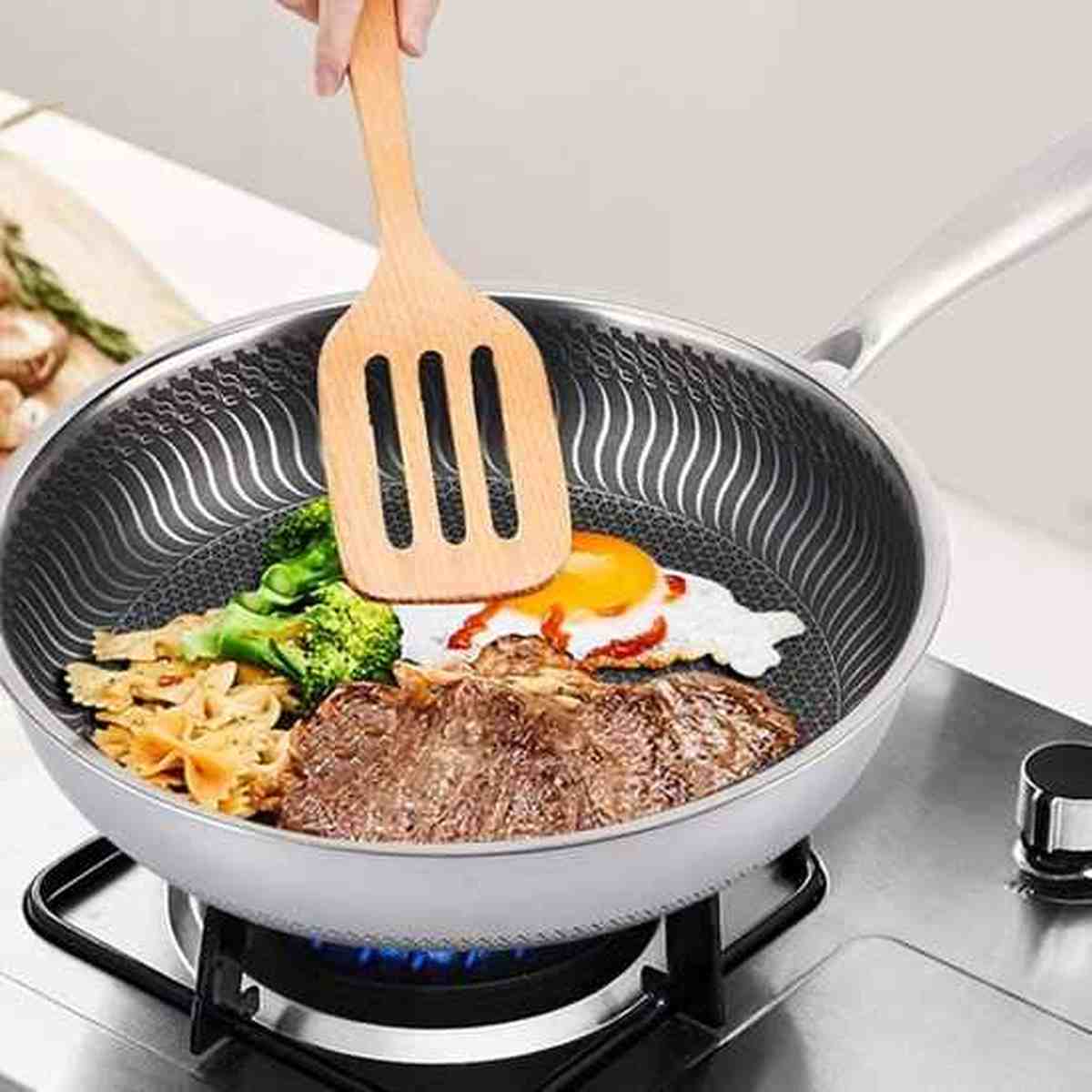 Poêle en acier inoxydable de qualité supérieure avec fond texturé, utilisée pour saisir de la viande et des légumes sur un feu à gaz.