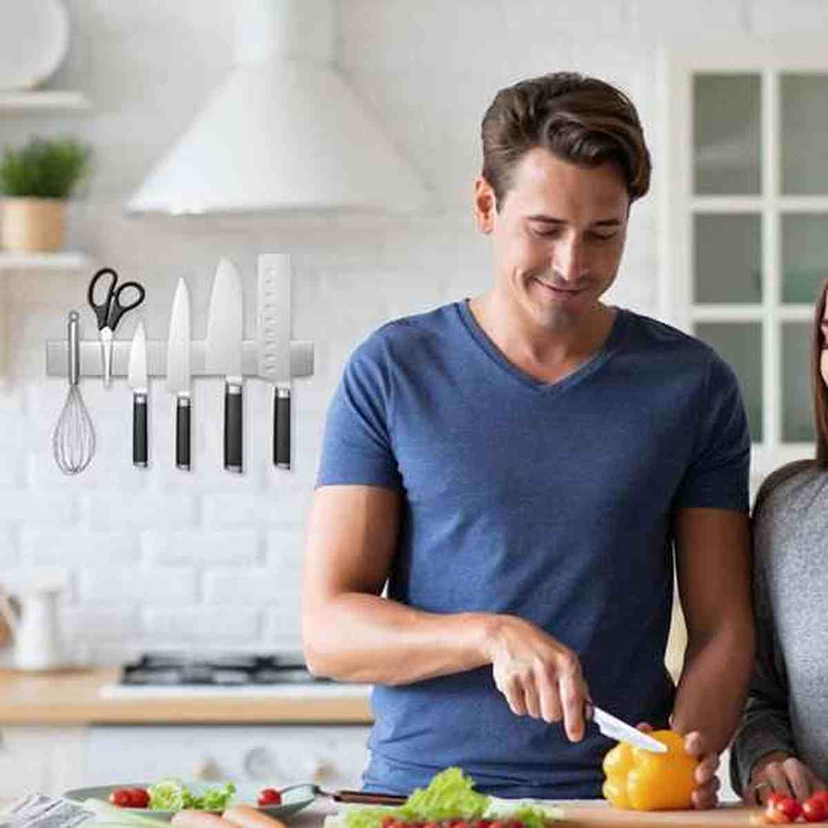 Homme préparant un repas avec un couteau de cuisine, avec une barre magnétique en inox fixée au mur pour un rangement organisé.