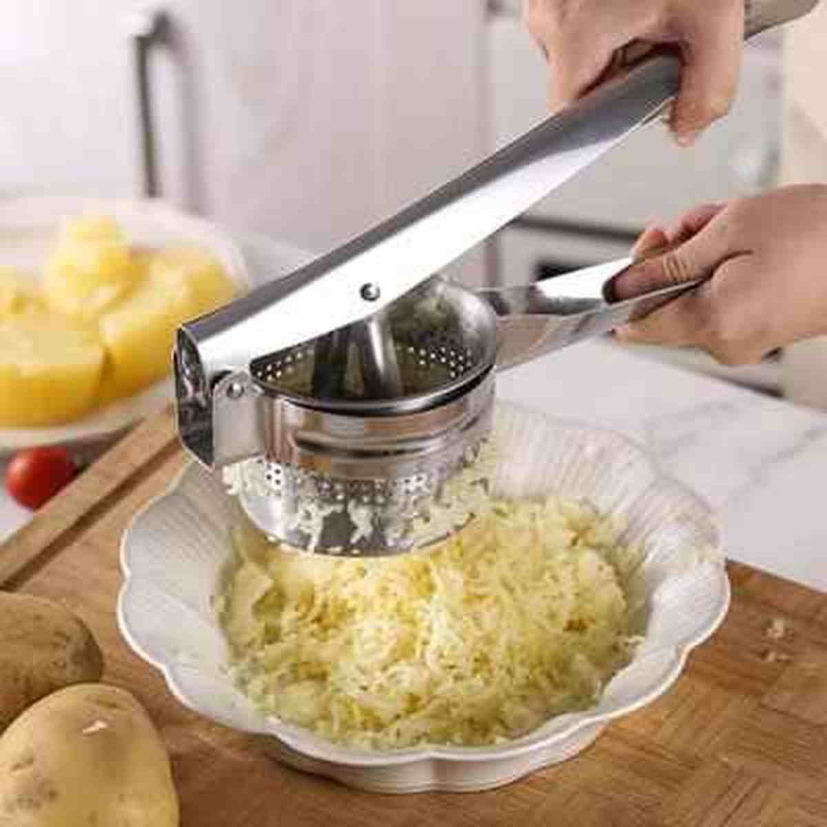Action de pressage de pommes de terre avec le presse-purée à levier en inox pour obtenir des filaments réguliers dans un plat.