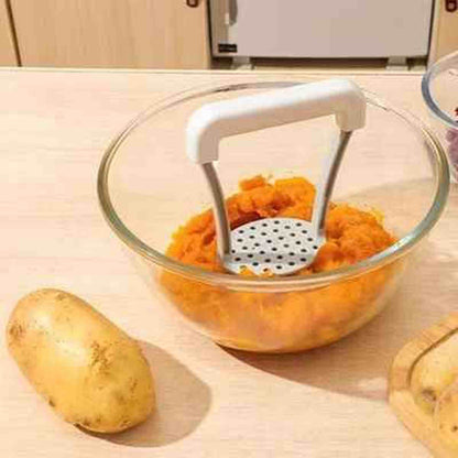 Presse-purée en acier inoxydable avec manche blanc ergonomique, posé dans un bol de purée de patates douces onctueuse.