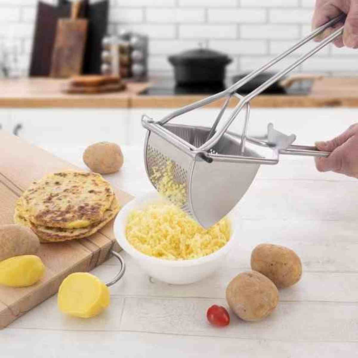 Presse-purée professionnel en inox extrudant des pommes de terre cuites pour une purée lisse, avec des légumes frais sur un plan de travail.
