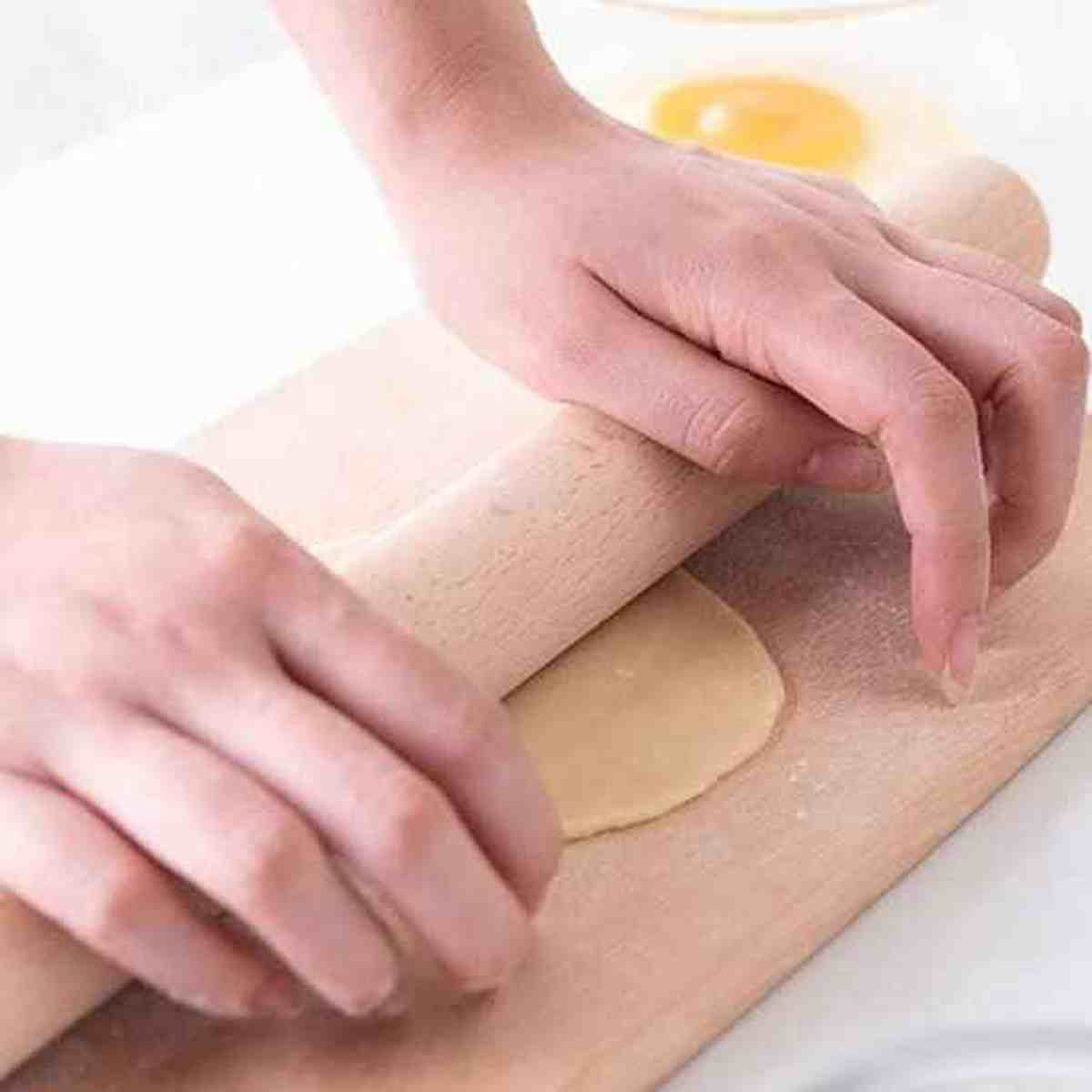 Gros plan de mains utilisant le rouleau à pâtisserie Artisan Pro en bois naturel pour étaler une pâte ronde sur une planche à découper