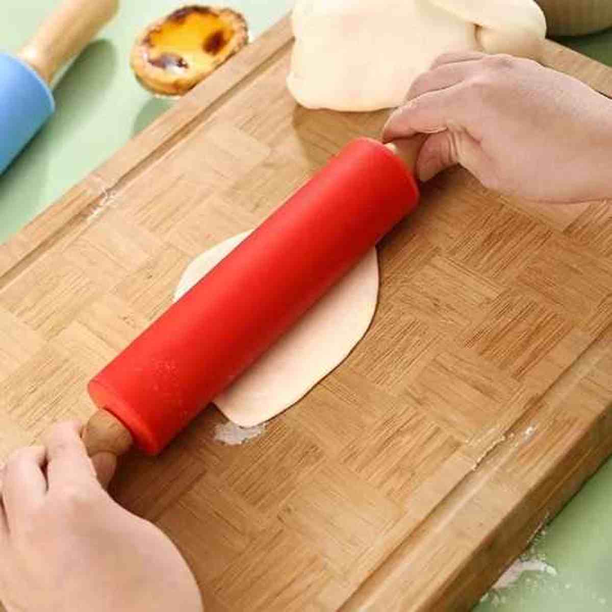 Rouleau à pâtisserie en silicone rouge antiadhésif étalant une pâte fine sur une planche en bois pour la confection de pâtisseries.