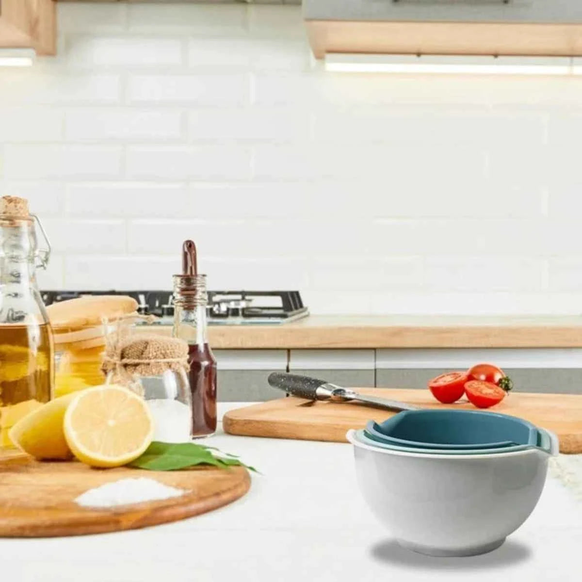 Trois bols de mélange empilables en plastique blanc et bleu posés sur un plan de travail de cuisine avec des ingrédients frais.