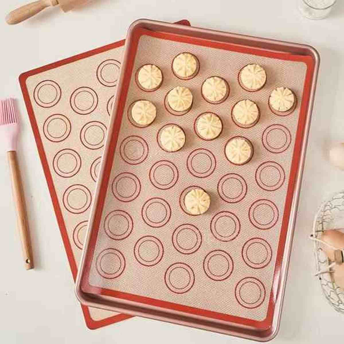 Tapis de cuisson en silicone beige avec repères circulaires pour macarons et pâtisseries, posé à côté d'un pinceau de cuisine sur un plan de travail.