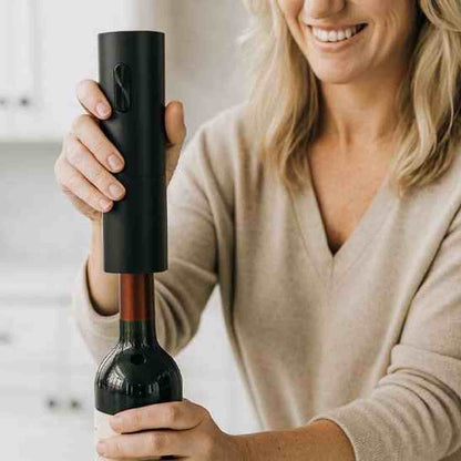Femme souriante utilisant le tire-bouchon électrique sur une bouteille de vin rouge, illustrant un débouchage rapide et sans effort