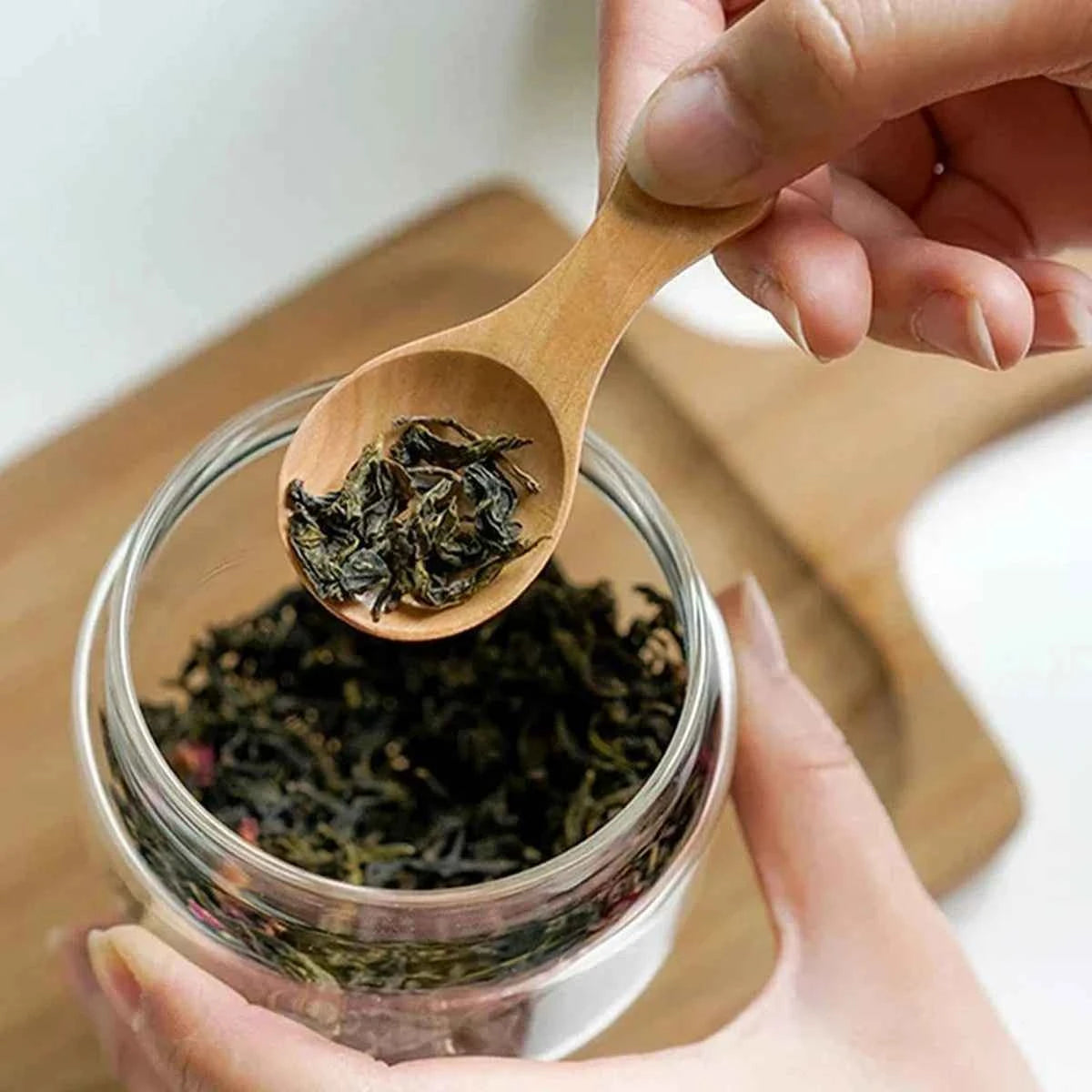 Utilisation d'une mini cuillère en bois naturel pour doser du thé en vrac dans un bocal en verre