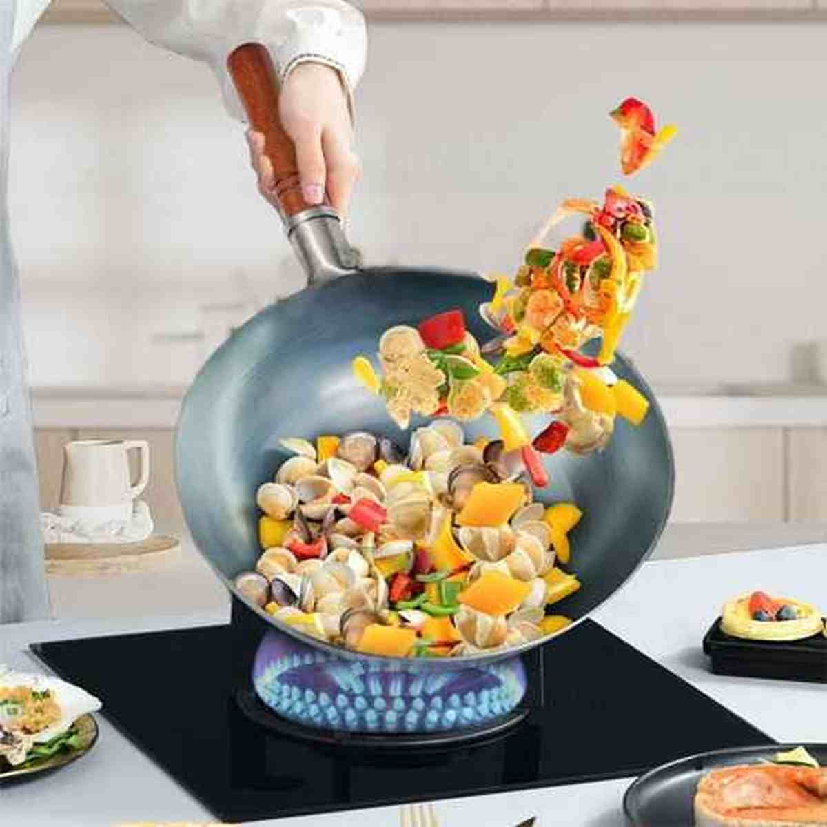 Wok en acier au carbone antiadhésif utilisé pour faire sauter des légumes et des fruits de mer sur une plaque à induction.