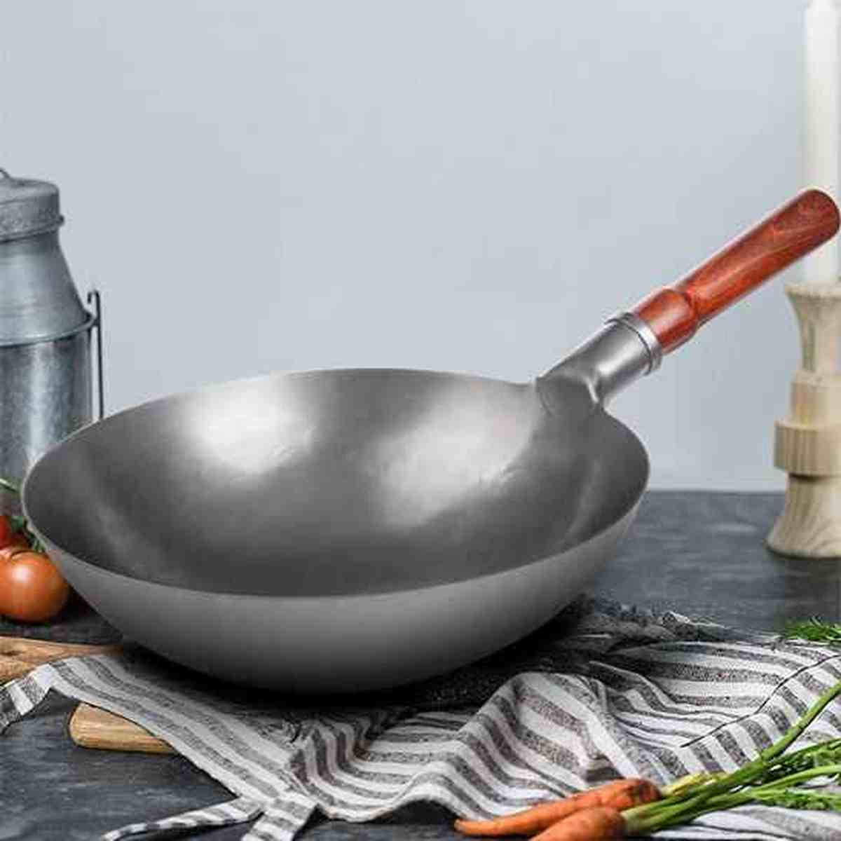 Wok professionnel en acier au carbone avec manche en bois ergonomique posé sur un plan de travail avec des légumes frais.